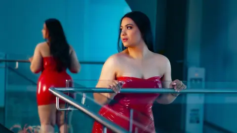 Elegant woman in a red latex strapless dress posing on a balcony with a moody blue aesthetic.