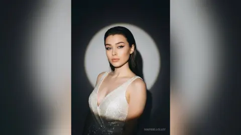 Elegant woman in a shimmering white sequin gown posing under dramatic studio spotlighting.