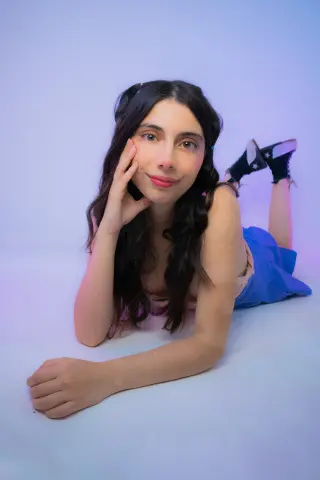 Young woman with long dark hair in a pink top and blue skirt lying on a light background with a dreamy mood.