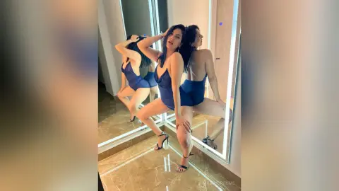 MaddyBrohms poses in a blue bodysuit and black heels, showing off her legs and curves in front of a mirror.