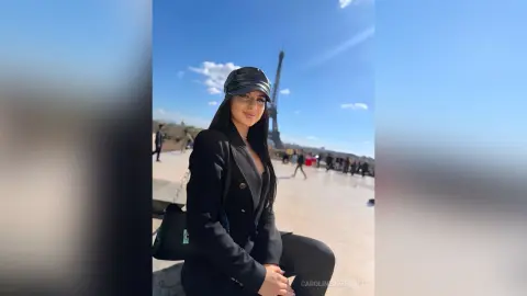 Stylish woman in a black blazer and leather cap smiling in front of the Eiffel Tower on a sunny day.