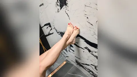 Close-up of bare feet against a modern white and black marble wall in a luxury bathroom setting.