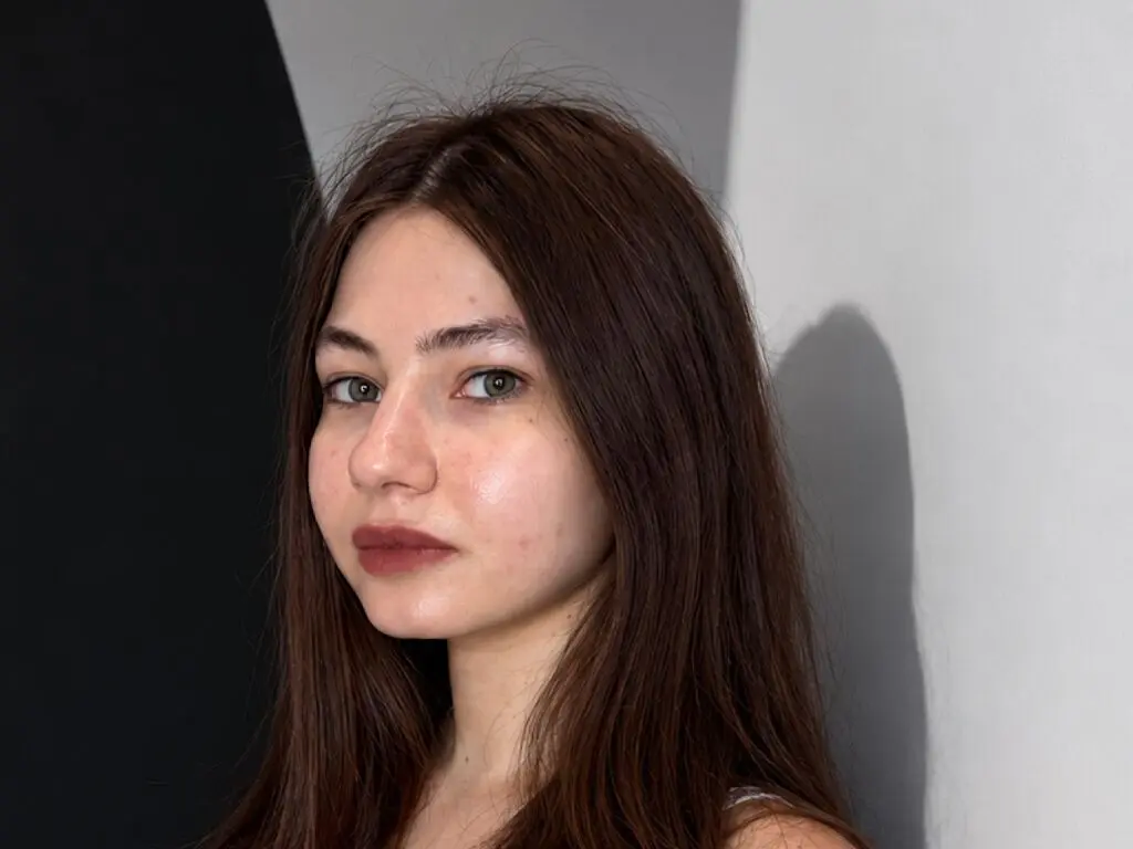 RoselynSvatek looks directly at the camera with long brown hair and dark red lipstick against a plain grey and black background.