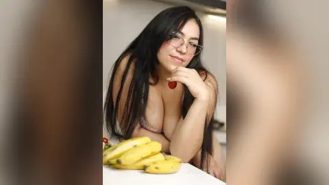 Young woman with long dark hair and glasses wearing a white bikini top in a bright indoor setting.