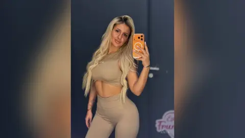 Anita poses for a mirror selfie wearing a tan two-piece crop top and matching leggings.