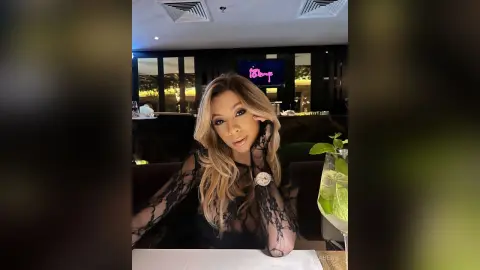 Glamorous woman in a black lace outfit enjoying a cocktail at a dimly lit upscale lounge.
