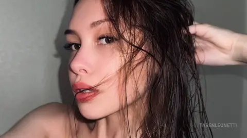 TarenLeonetti poses with her wet, dark hair pulled back, showing her face and bare shoulders against a plain wall.