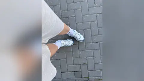 EmilyGiffin wearing a white dress and white sneakers, standing on a grey brick pavement.