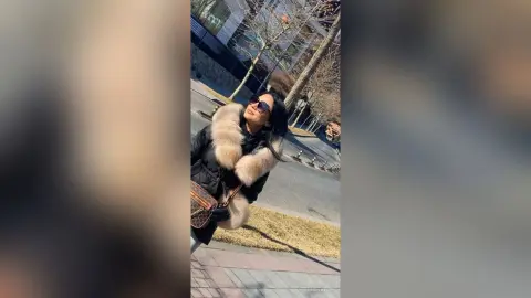 Stylish woman in a black winter coat and fur collar wearing sunglasses on a sunny city street.