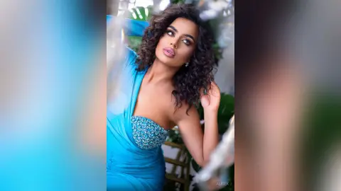 Glamorous woman in a sparkling blue sequin gown posing with a confident expression in a lush garden setting.