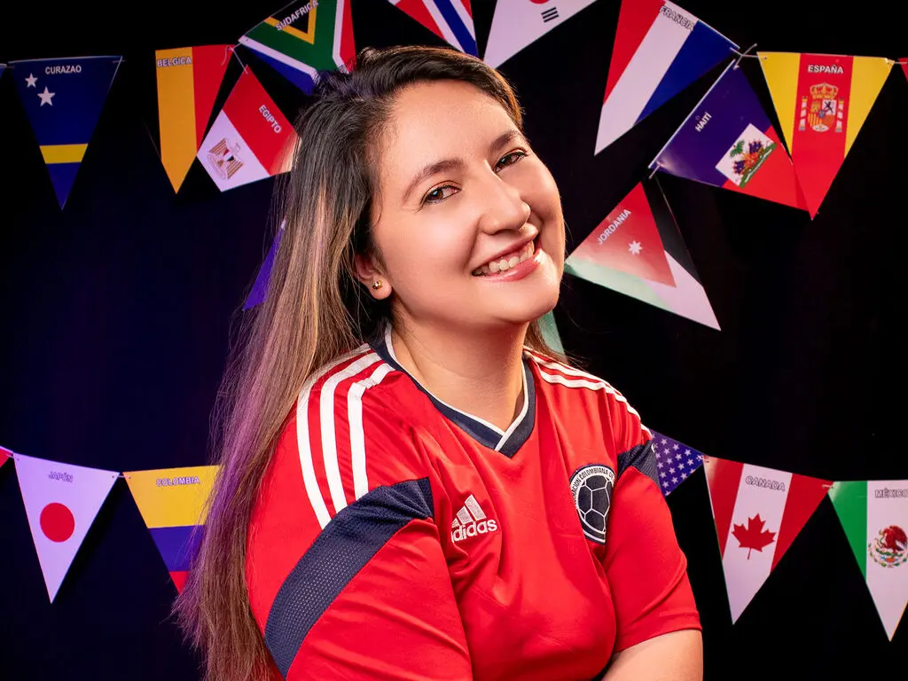 HarperEvans smiles wearing a red Adidas soccer jersey against a dark background decorated with colorful international flags.