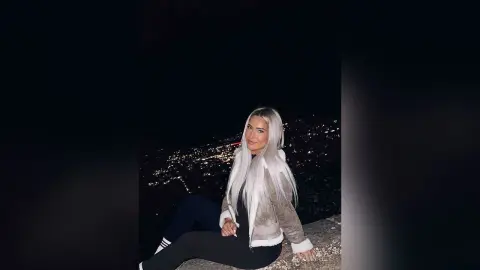 Woman in a cozy beige jacket sitting against a glowing city skyline at night.