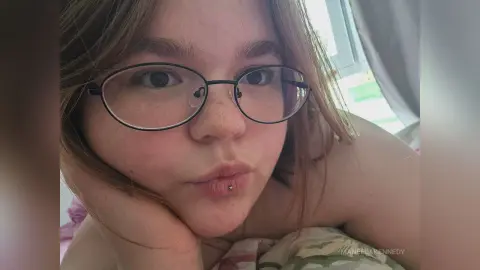 ManeelaKennedy wearing glasses and looking at the camera while resting her chin on her hand.
