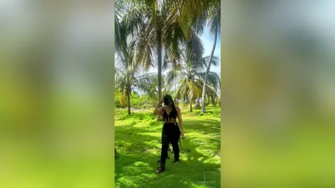 Stylish woman in a black summer outfit walking through a sunny tropical palm tree garden.