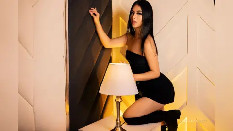 EmmaFiorelli poses in a black strapless dress against a dark headboard and white paneled wall.