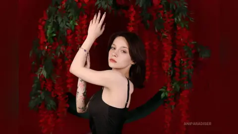 Young woman in a black tank top posing gracefully against a lush red floral backdrop in a moody setting.