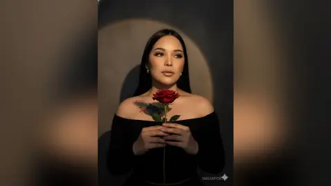 Elegant woman in a black off-the-shoulder dress holding a single red rose in moody, dramatic lighting.