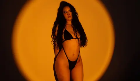 Woman in black bikini posing against a warm golden circular light backdrop in a moody studio setting.
