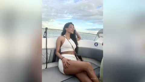 Smiling woman in a white summer outfit relaxing on a boat during a sunny ocean cruise.