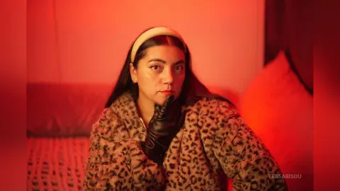 Stylish woman in leopard print coat and black gloves posing thoughtfully in warm red lighting.