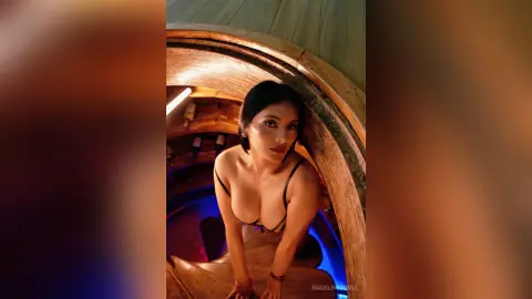Young woman in a black bikini top relaxing on a wooden staircase in warm, moody lighting.