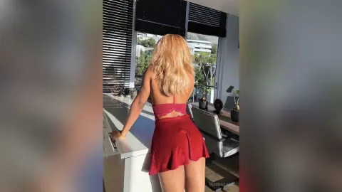 Blonde woman in a red mini dress standing by a window in a bright, modern room.