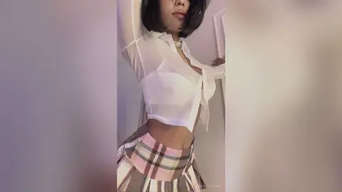 Woman in a white sheer blouse and plaid skirt posing in a bright indoor setting with a soft mood.