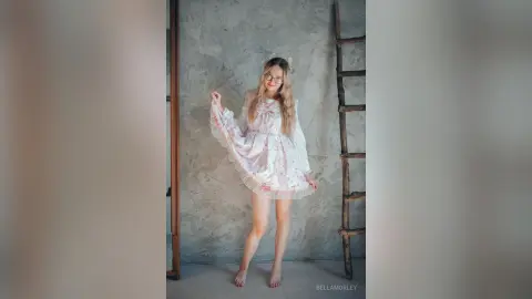 Young woman in a white floral cottagecore dress posing in a minimalist studio with a rustic wooden ladder.