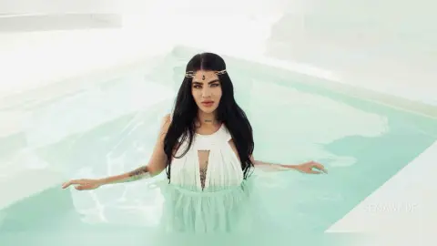 Ethereal woman in a white flowing dress and gold headpiece relaxing in a bright turquoise pool.