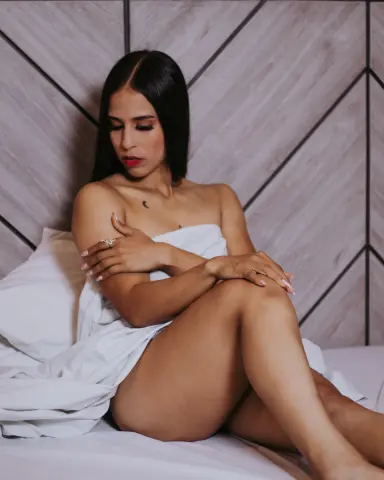 Young woman in white sheets sitting on a bed against a modern wood paneled wall in a serene mood.