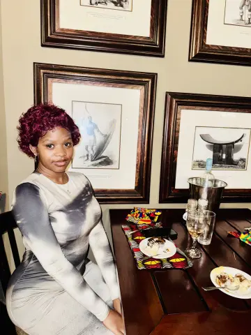 Young woman with red hair in a grey dress sitting at a restaurant table with framed art on the wall.