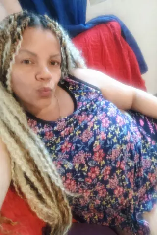 Woman with long blonde braids wearing a floral print tank top relaxing in a cozy indoor setting.