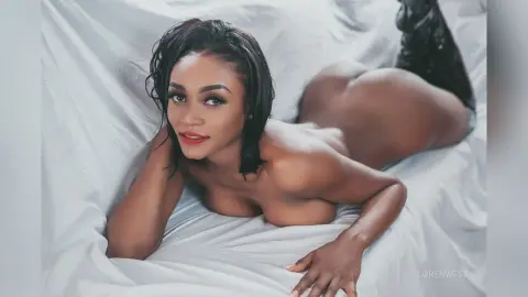 Nude woman lying on white bedsheets in a soft, intimate bedroom setting.