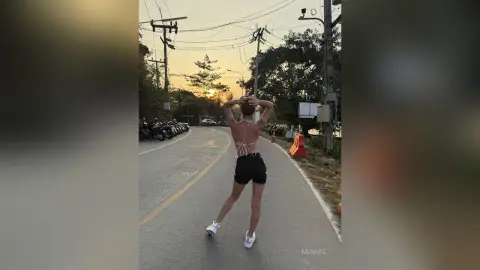 Fit woman in black shorts and white bikini top posing on a road during a golden sunset.