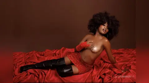Glamorous woman in red sparkly shorts and gloves reclining on red satin fabric in a moody studio setting.