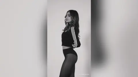 Stylish woman in black athletic crop top and leggings posing against a minimalist studio background.