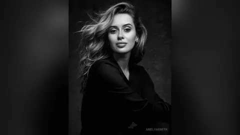 Elegant woman with flowing wavy hair wearing a black blouse in a moody black and white portrait.