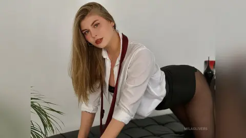 Blonde woman in a white button-down shirt and black skirt posing elegantly in a bright minimalist room.