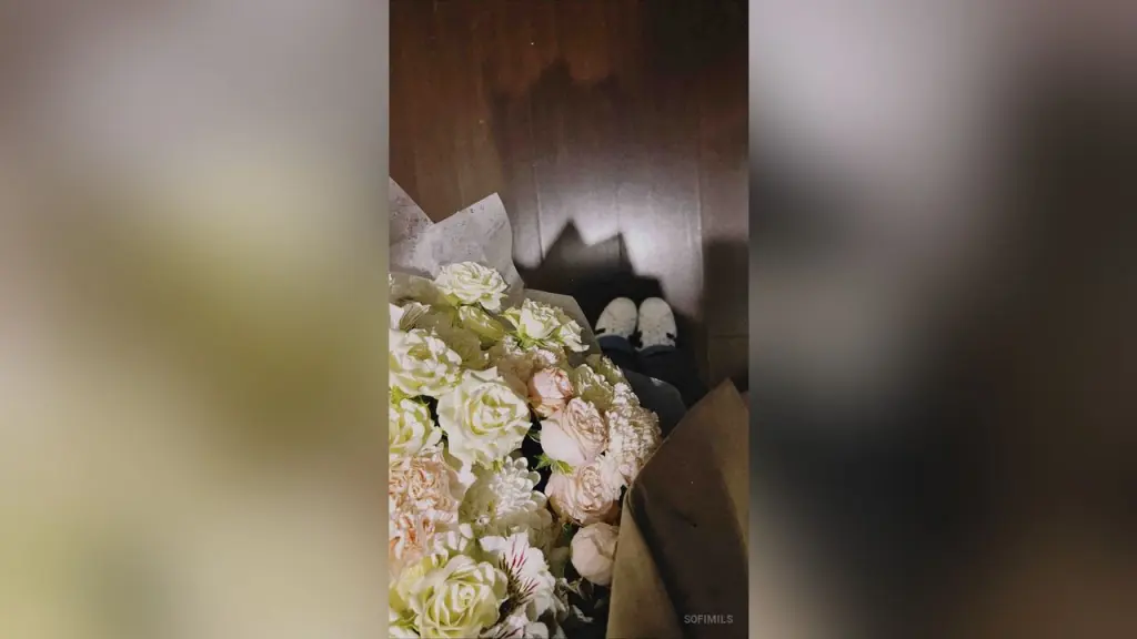 SofiMils β SofiMils holds a large bouquet of white and light pink roses against a dark wooden floor.