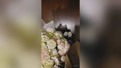 Large bouquet of white and peach roses wrapped in brown paper on a dark wooden floor.