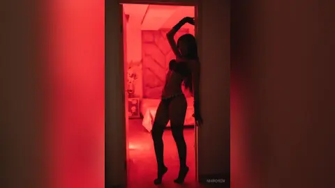 Slim woman in black lingerie posing in a room with moody red lighting.