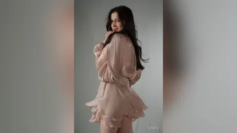 Smiling woman in a flowing blush pink satin dress posing in a minimalist studio setting.