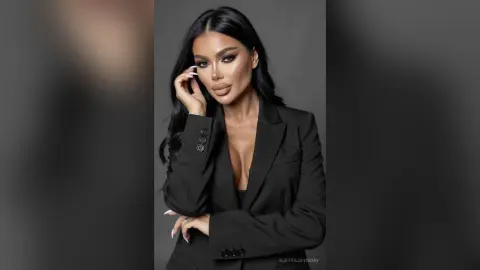 Glamorous woman with long dark hair wearing a chic black blazer in a professional studio setting.