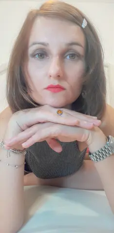 Woman in a black ribbed top resting her chin on her hands in a bright, cozy indoor setting.