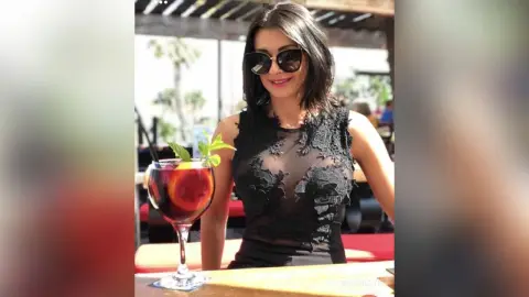 Stylish woman in a black lace sleeveless top enjoying a refreshing summer cocktail at an outdoor cafe.