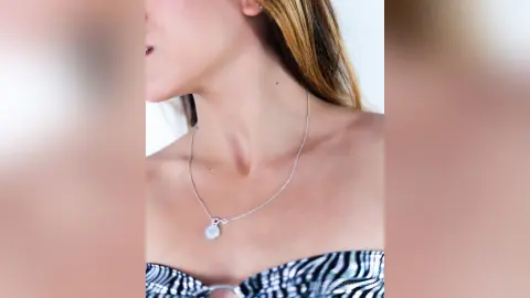 Woman in a zebra print top wearing a delicate silver coin pendant necklace against a bright background.