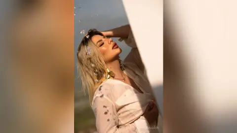 Blonde woman in a white blouse posing elegantly in warm sunlight for a dreamy, aesthetic portrait.