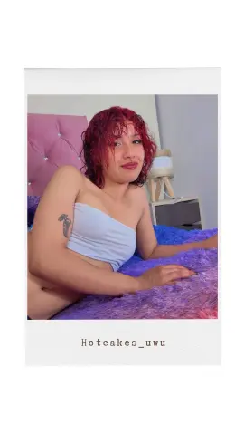 Red-haired woman in a white tube top relaxing on a purple shag rug in a cozy bedroom setting.