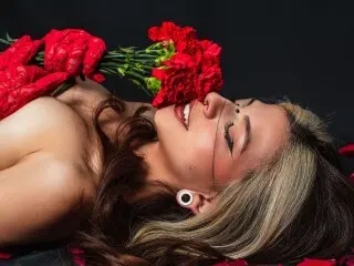 Smiling woman with long wavy hair lying down holding a bouquet of red carnations in a moody studio setting.