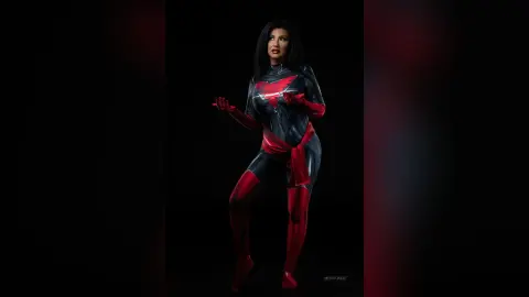 MissyJolie poses in a tight red and black bodysuit against a black background.
